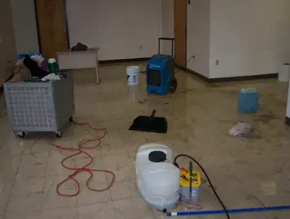 Dehumidifier, air mover and cleaning gear set up in a room with a wet tile floor